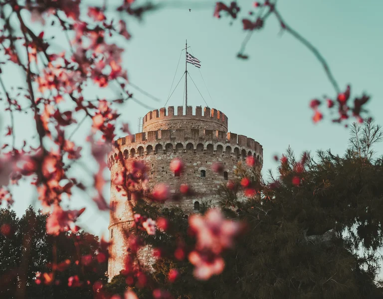 Round stone tower with a flag, framed by pink blossoms and green foliage.