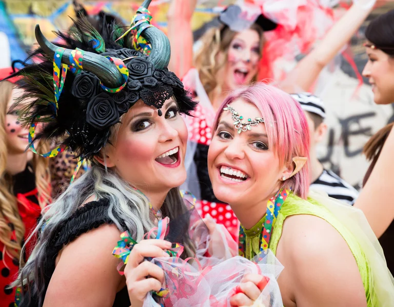 Two women in colorful, festive costumes smiling at a parade or party.