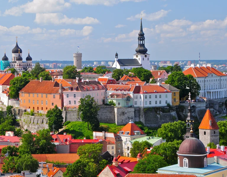 Colorful medieval cityscape with red rooftops, church spires, and lush green trees