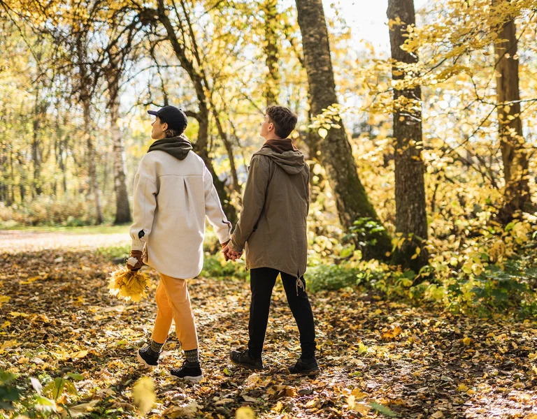 Two people holding hands, walking through a sunlit autumn forest.
