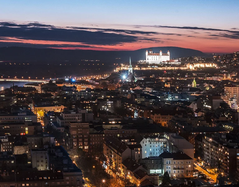 Cityscape at dusk with illuminated buildings and streets, sky showing the last light of sunset.