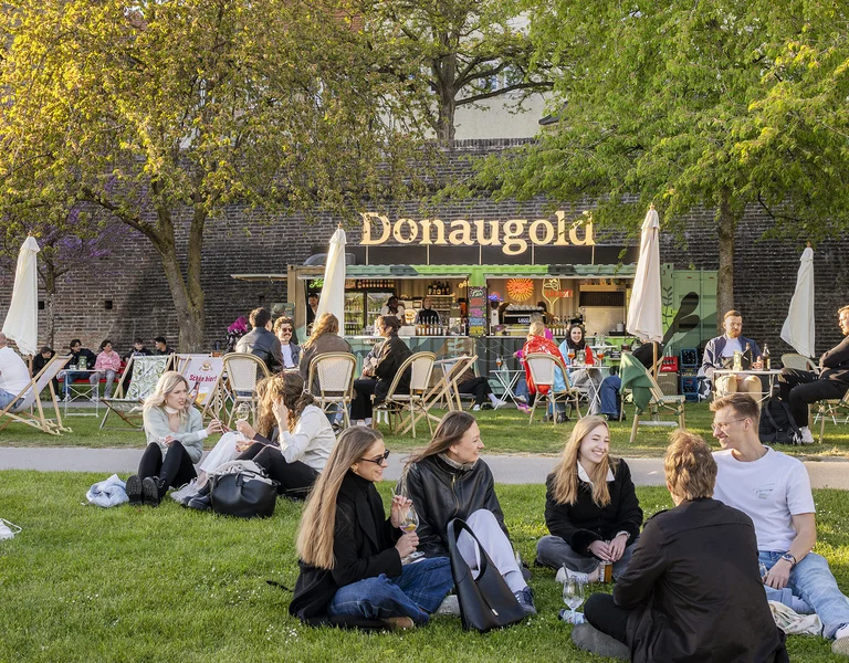 Groups of people relaxing on a grassy lawn outside a café on a sunny day.