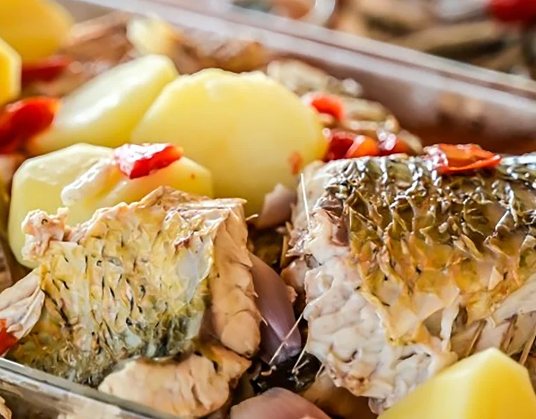 Baked fish with potatoes and red peppers in a glass dish.