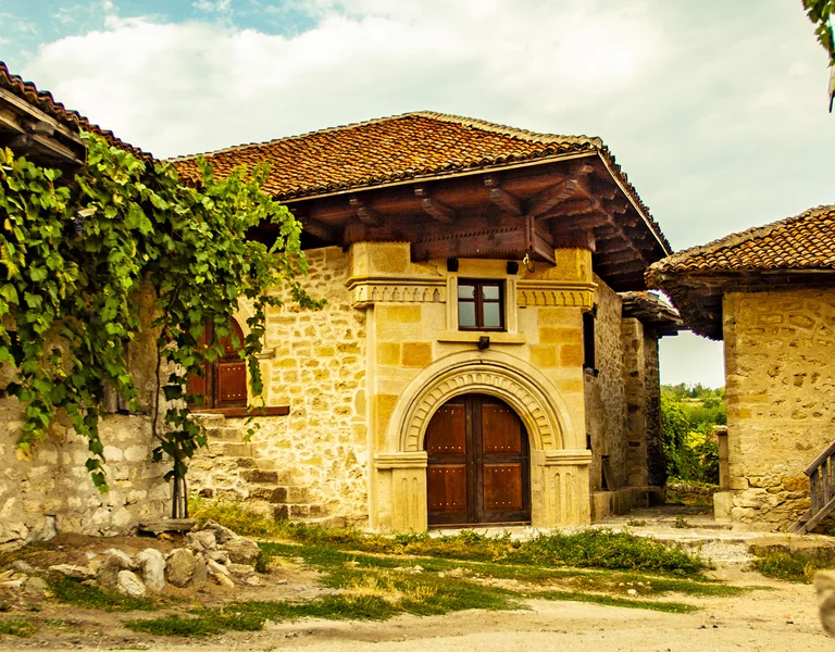 Sunlit stone courtyard with vine-covered walls and rustic wooden doors.