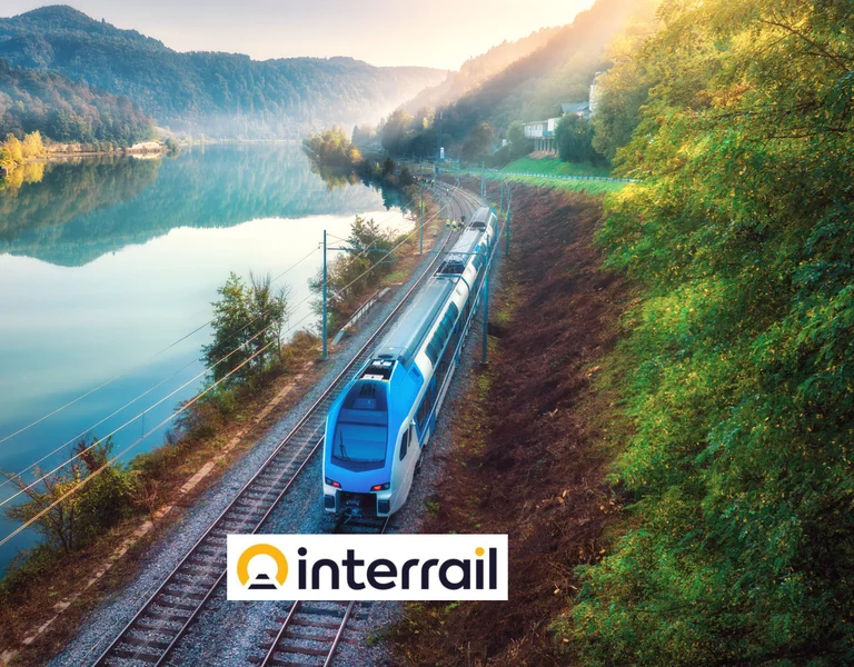 Um trem moderno viaja ao longo de uma trilha à beira do lago ao amanhecer, logotipo do interrail na parte inferior.