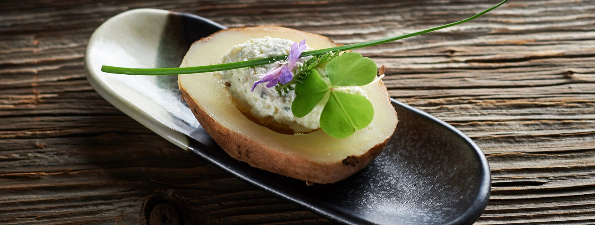 Find out how sophisticated a boiled potato can be, artfully topped with a dollop of soft cheese and garnished elegantly with a fresh herb sprig and a delicate edible flower.