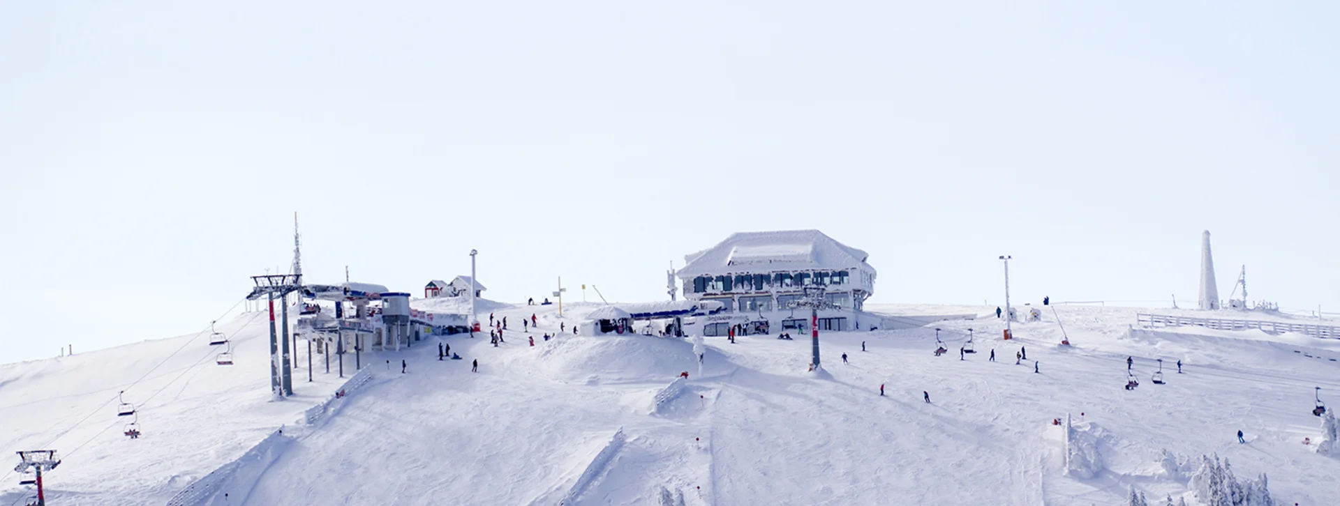 Snow-covered ski slope in Serbia during winter with skiers, lift chairs, and a lodge at the peak.