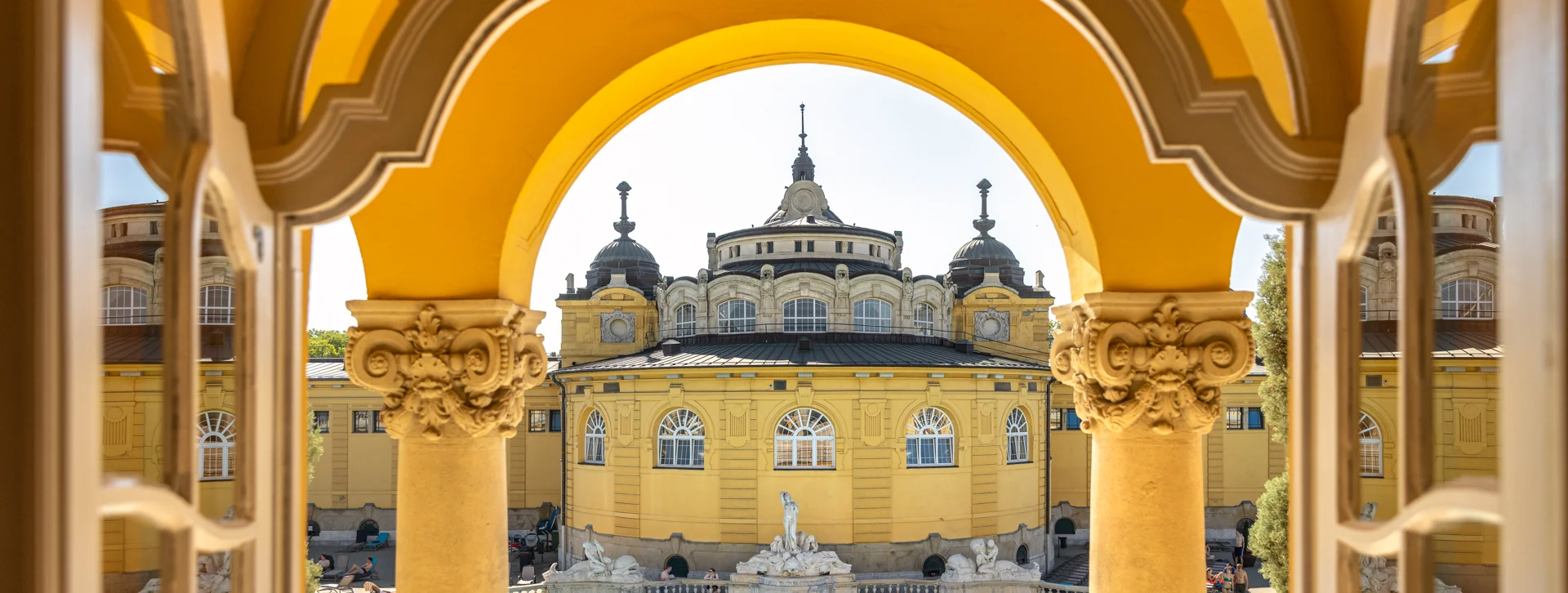 Elegant yellow building with domes viewed through an ornate yellow archway over a bright blue pool.