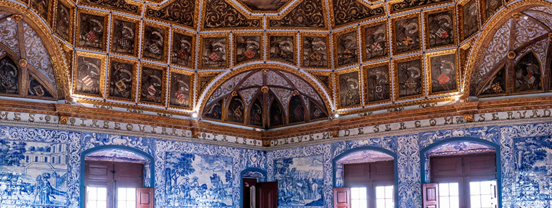 Ornate room with blue azulejo tile walls, gilded coffered ceiling, and painted scenes.