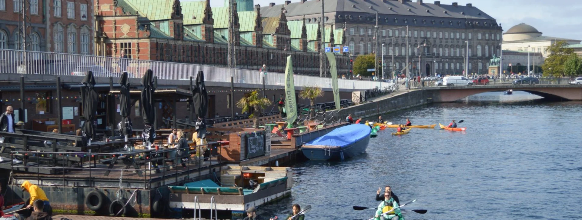 Multiple kayaks in Copenhagen’s canal with participants paddling, surrounded by historic buildings and blue skies.