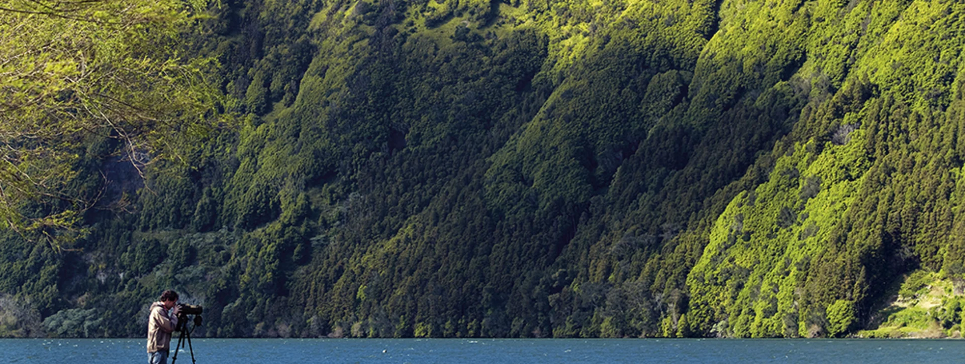 Person photographing a lake surrounded by lush green hills on São Miguel Island, Azores