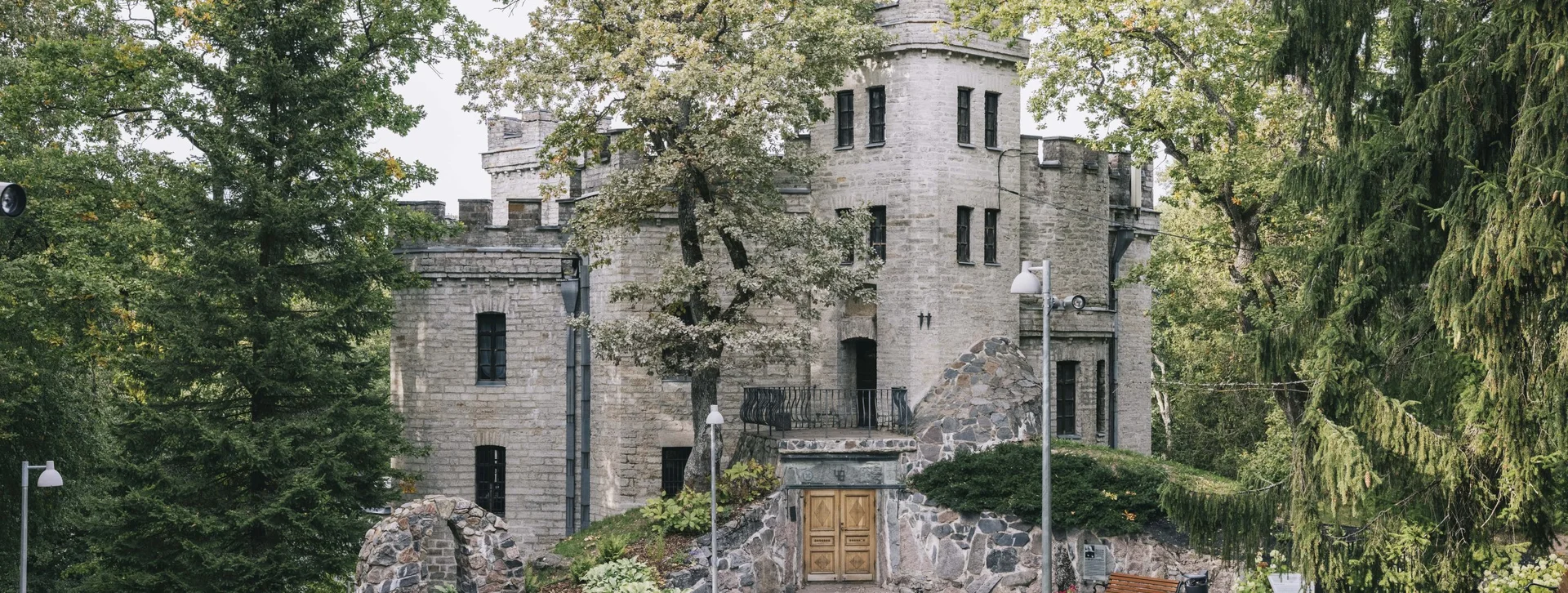 Historic stone castle surrounded by trees and greenery, with a cobblestone path leading to its wooden entrance door.