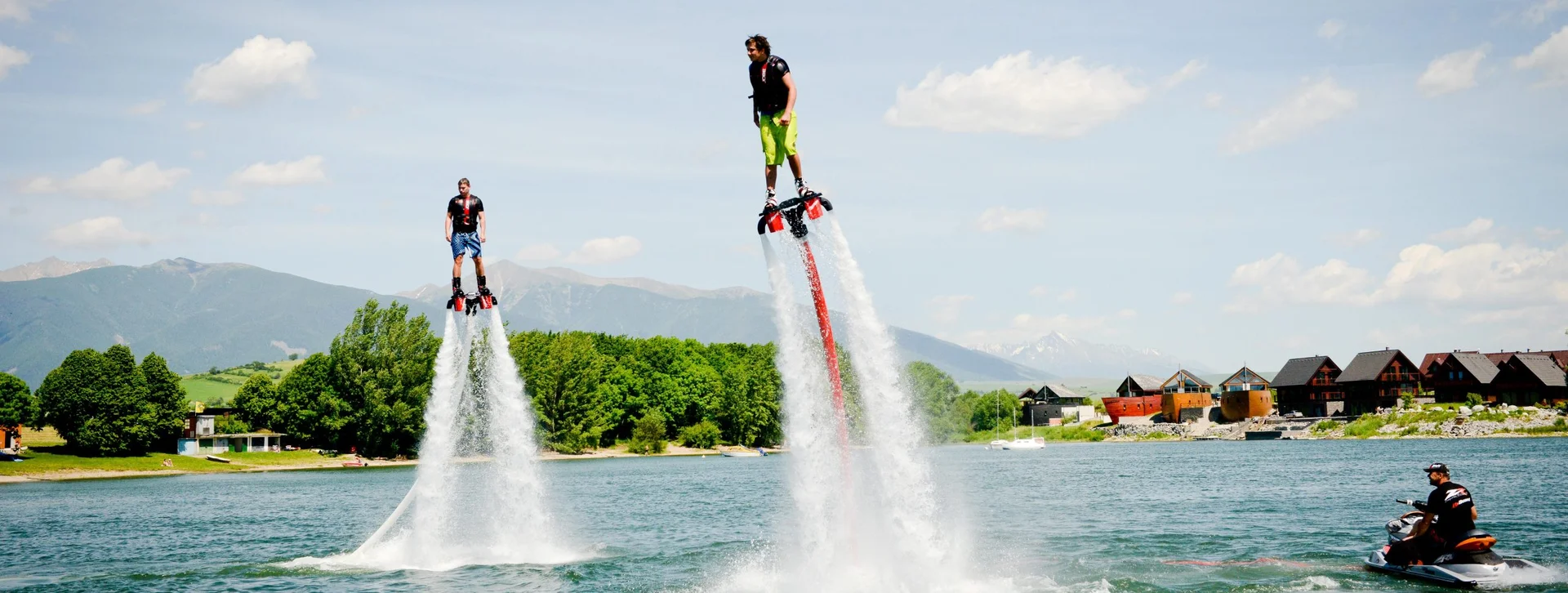 Two men flyboarding on a lake with mountains in the background.