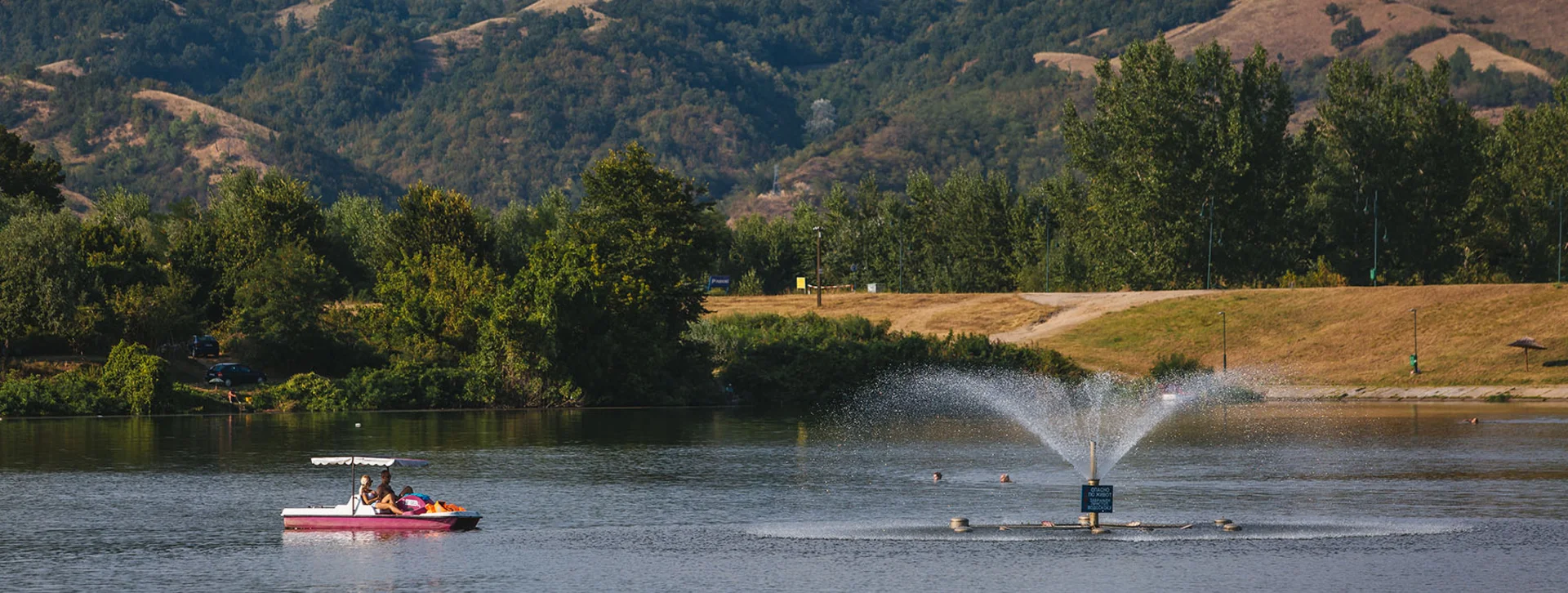 Fountain and paddle boat on Silver Lake with forested hills in the background.