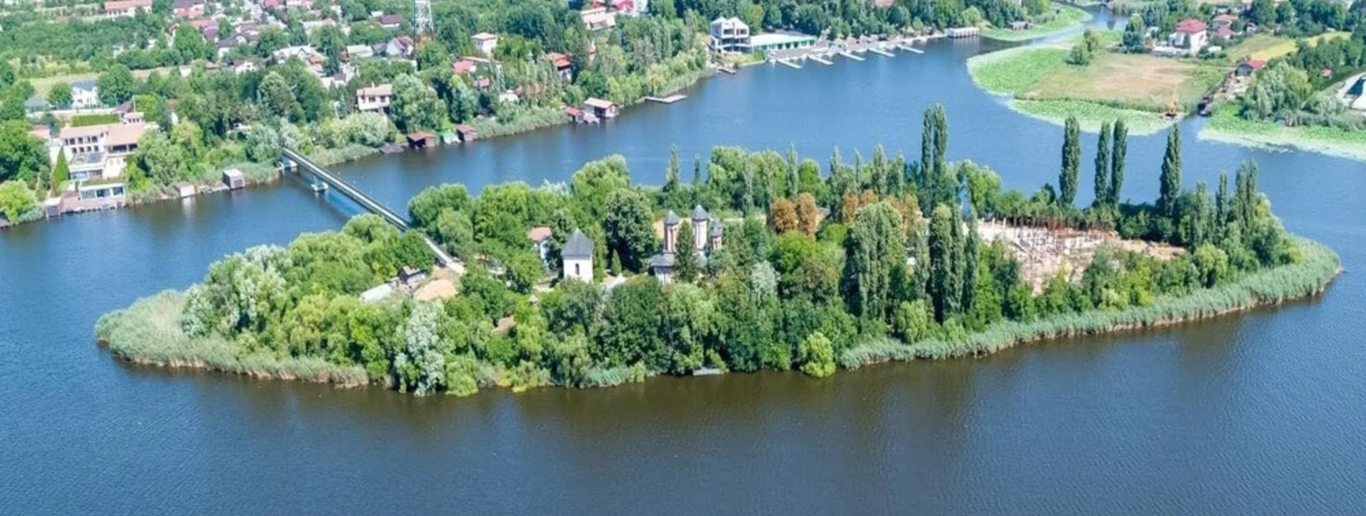 Aerial view of Snagov Lake with a green island and surrounding town..
