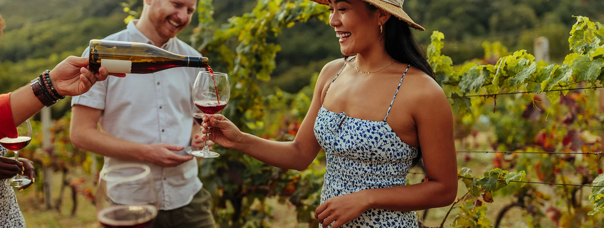 Unrecognizable man pouring red wine to asian woman in vineyard who came here with friends