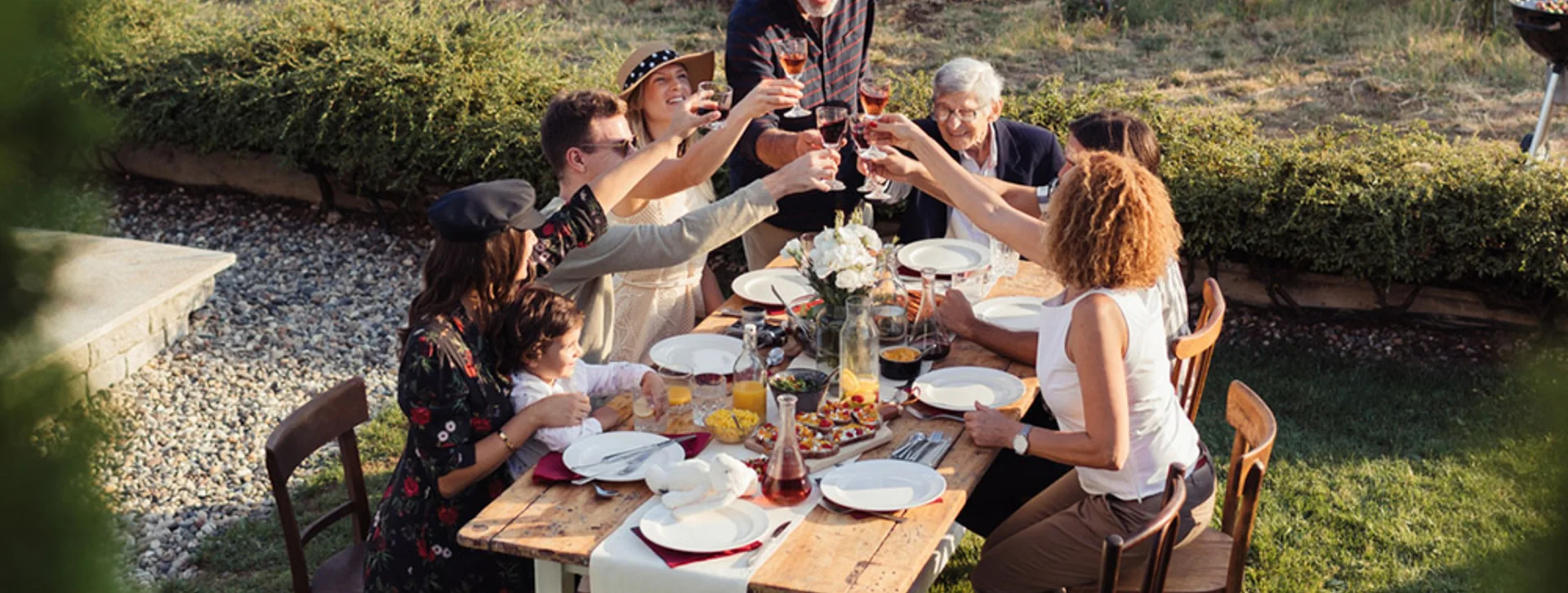 Family gathered outdoors in a vineyard in Serbia, raising glasses for a celebratory meal.