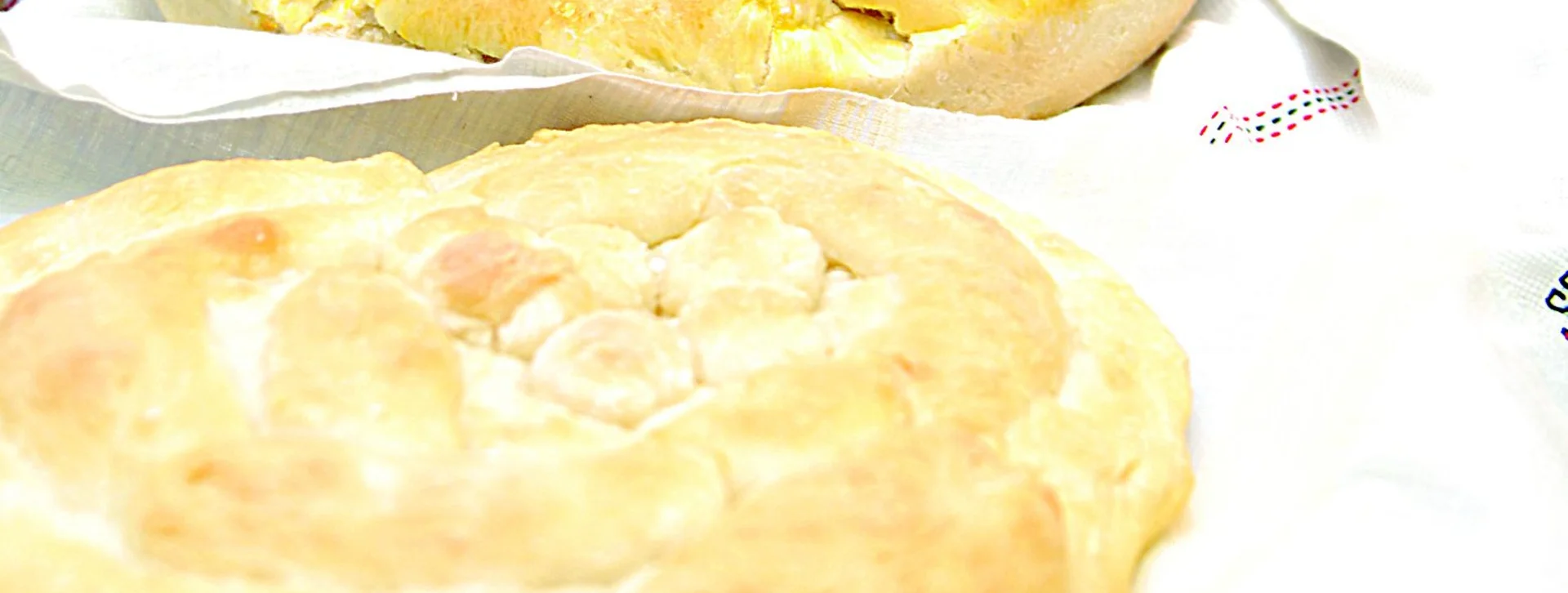 Traditional Bulgarian round bread, freshly baked and golden, served on a festive table with ceramic dishes and homemade wine.