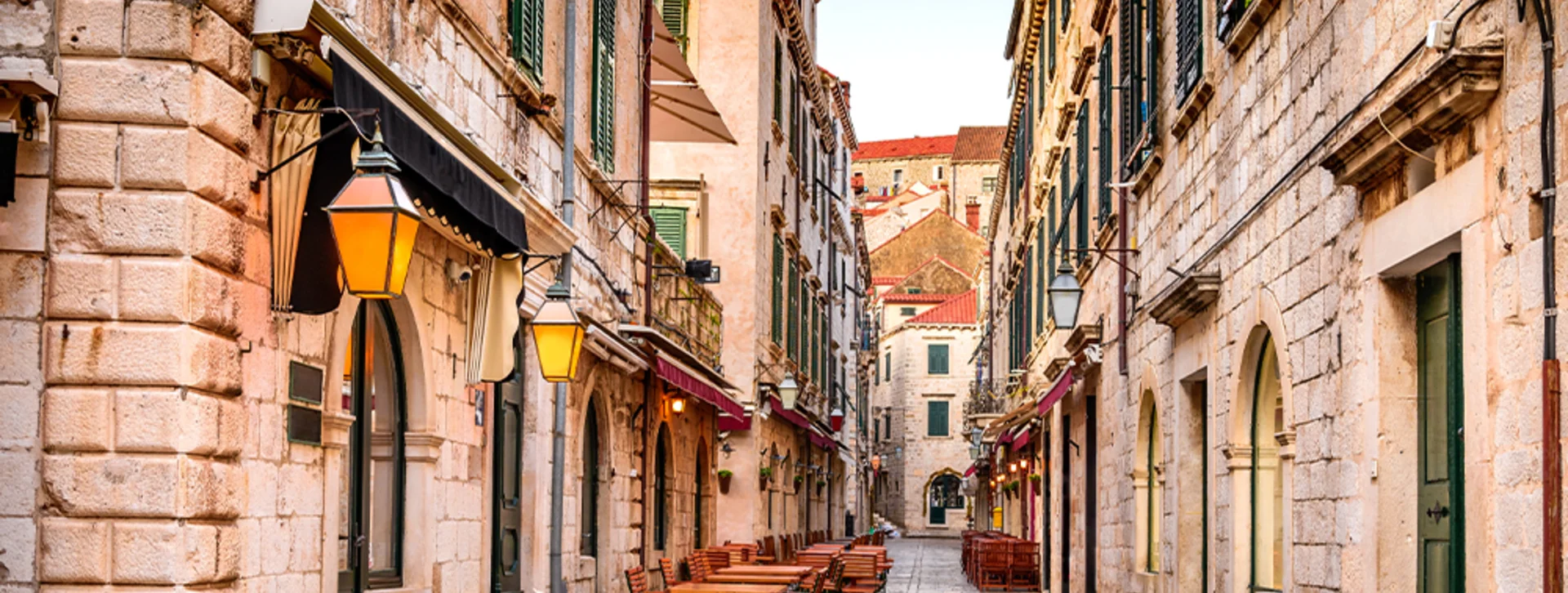 Outdoor café tables and chairs set under awnings along a narrow stone‑paved street in the Old Town of Dubrovnik.