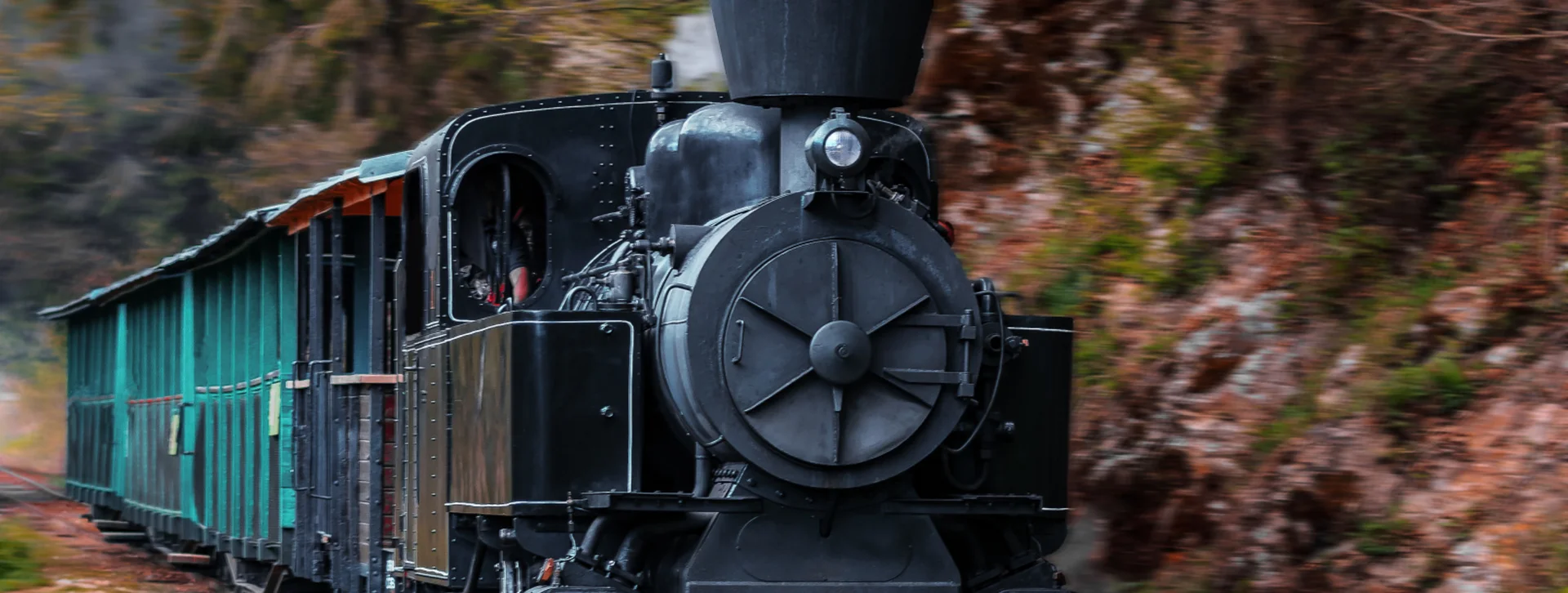 Steam locomotive with black smoke pulling green passenger cars through a forested area.