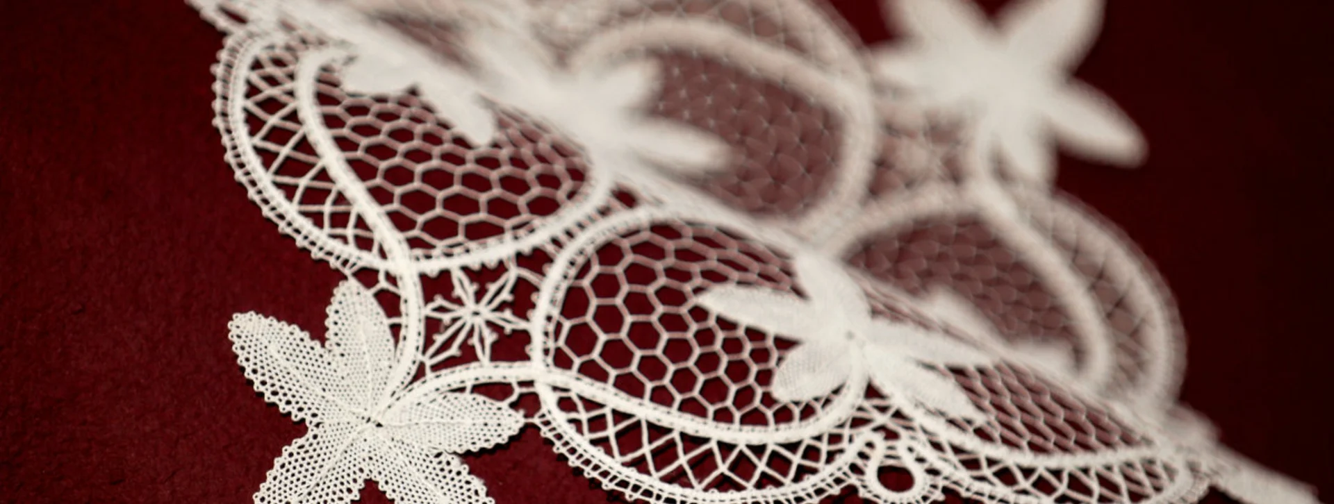 Delicate white lace with floral patterns on a deep red background.