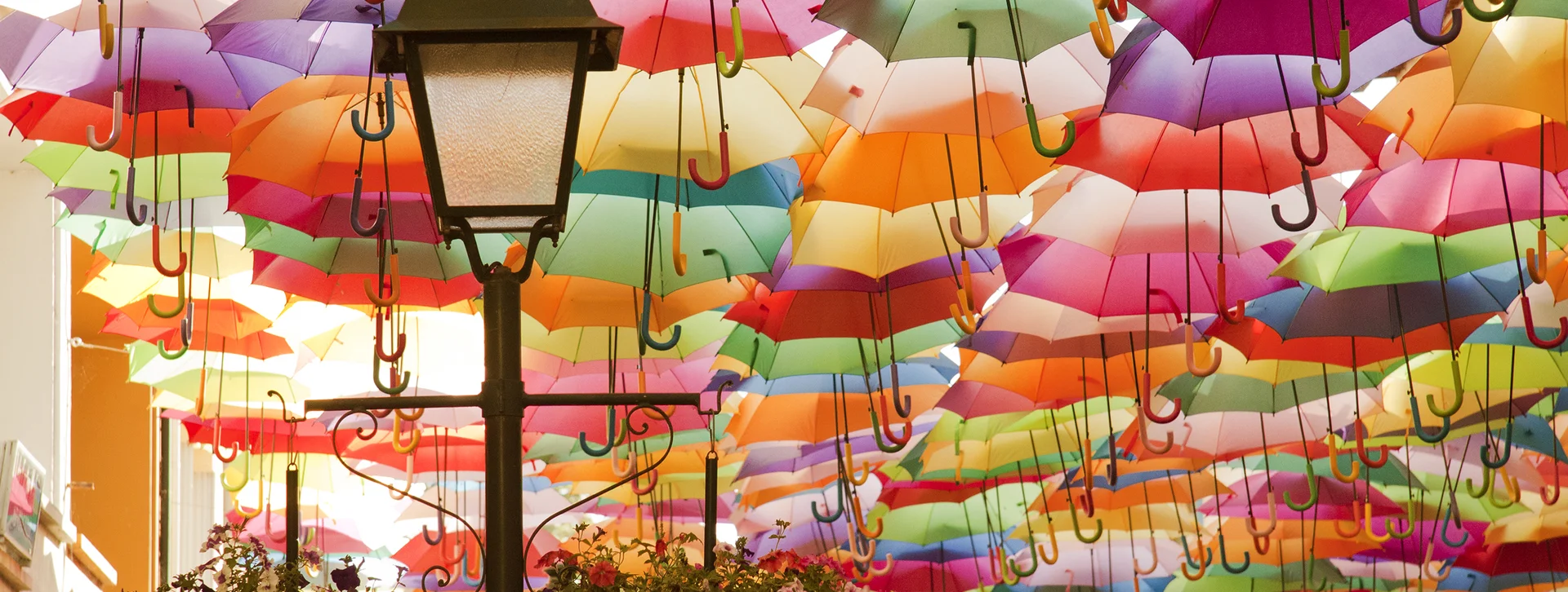 Colorful umbrellas suspended above a street with a lamp post and hanging flower baskets.