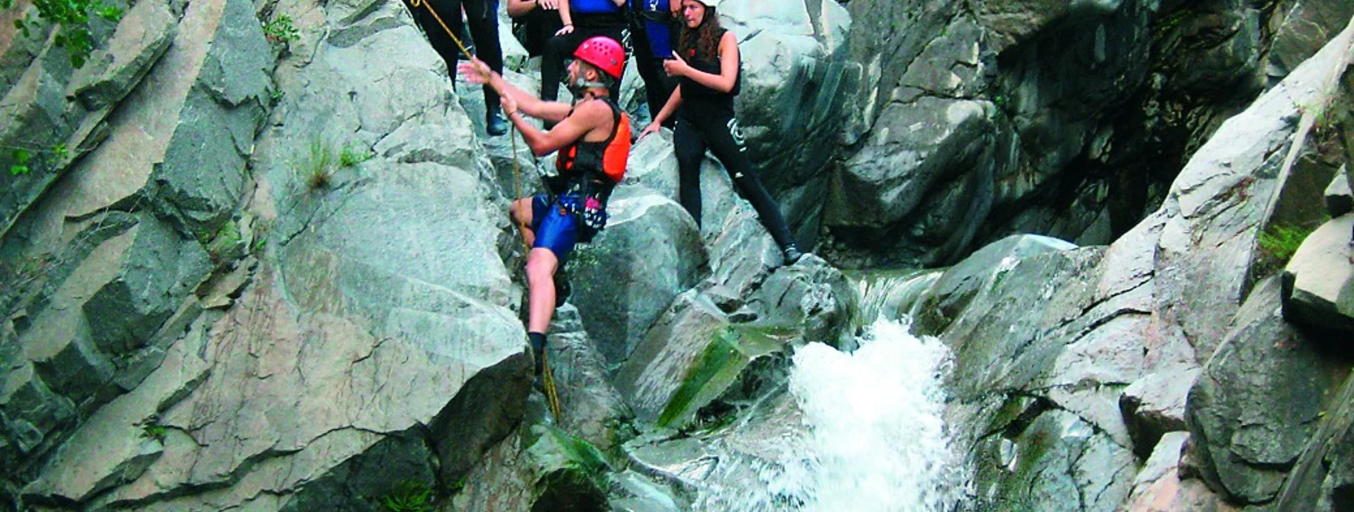 Group of people in helmets and vests climbing a rocky waterfall.