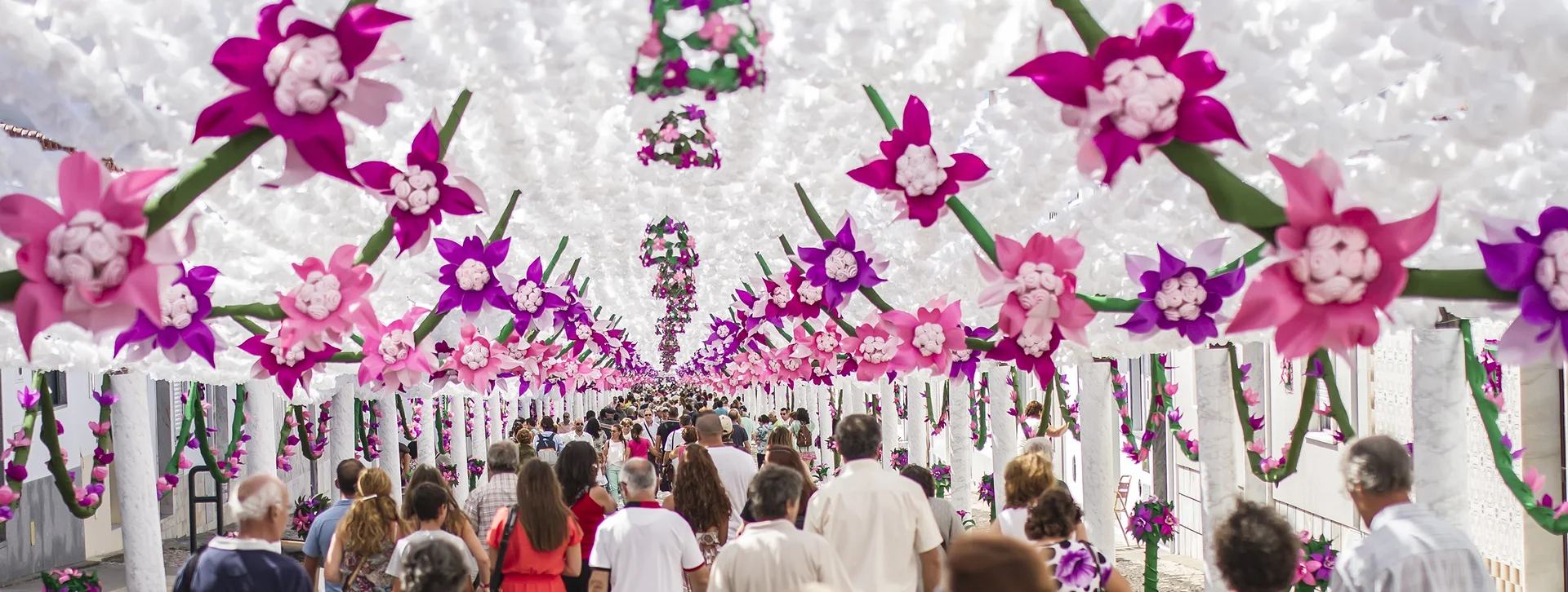 Crowd walking under a canopy decorated with large pink and purple flowers.