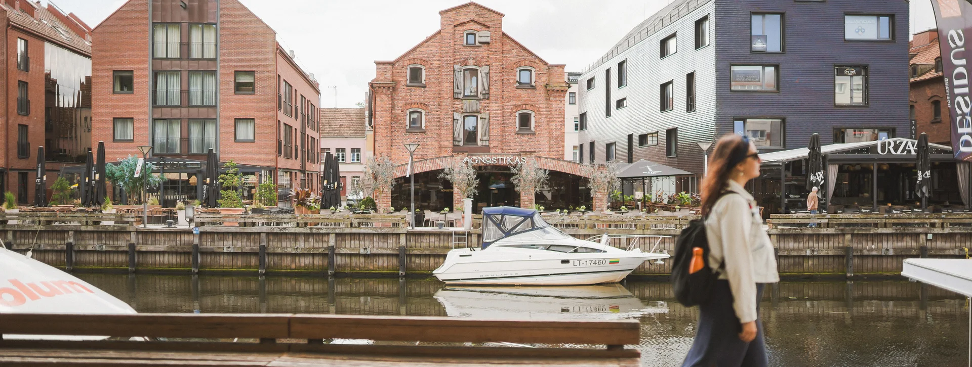 Woman walking by a canal with modern and historic buildings and boats in the background.