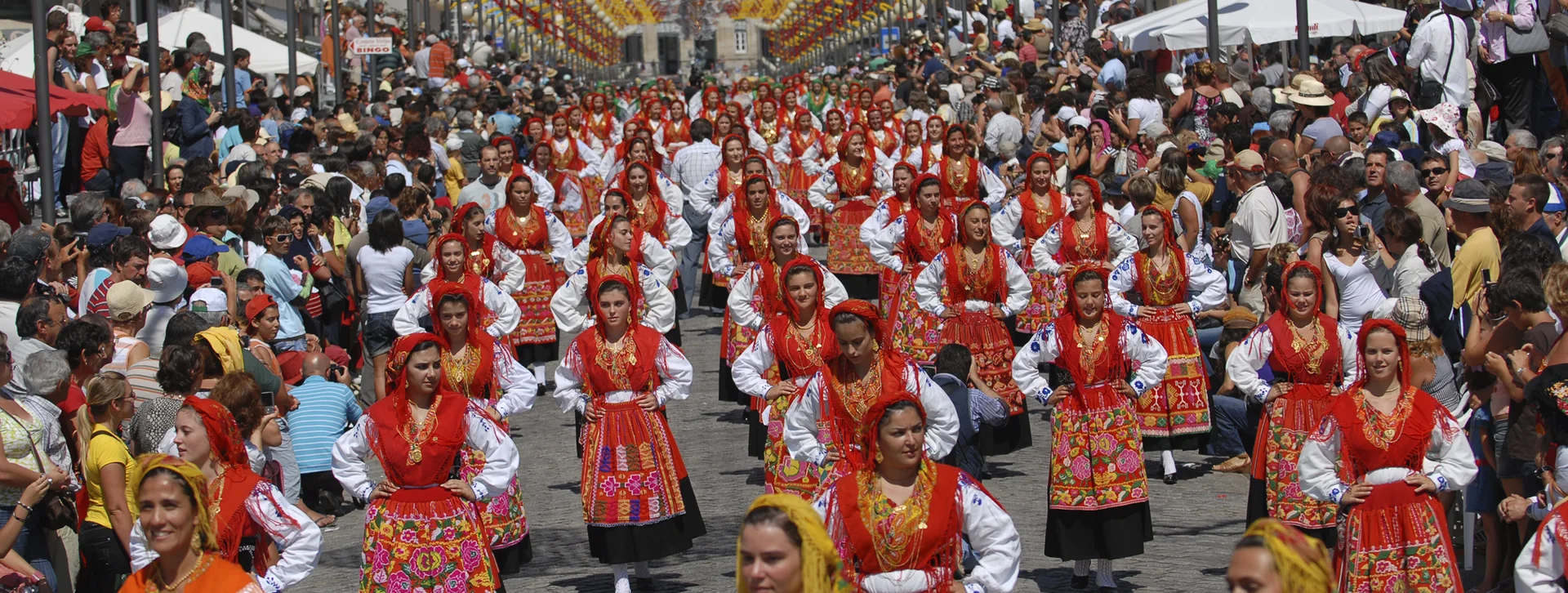 Women in colorful traditional dress perform in a crowded street festival parade.