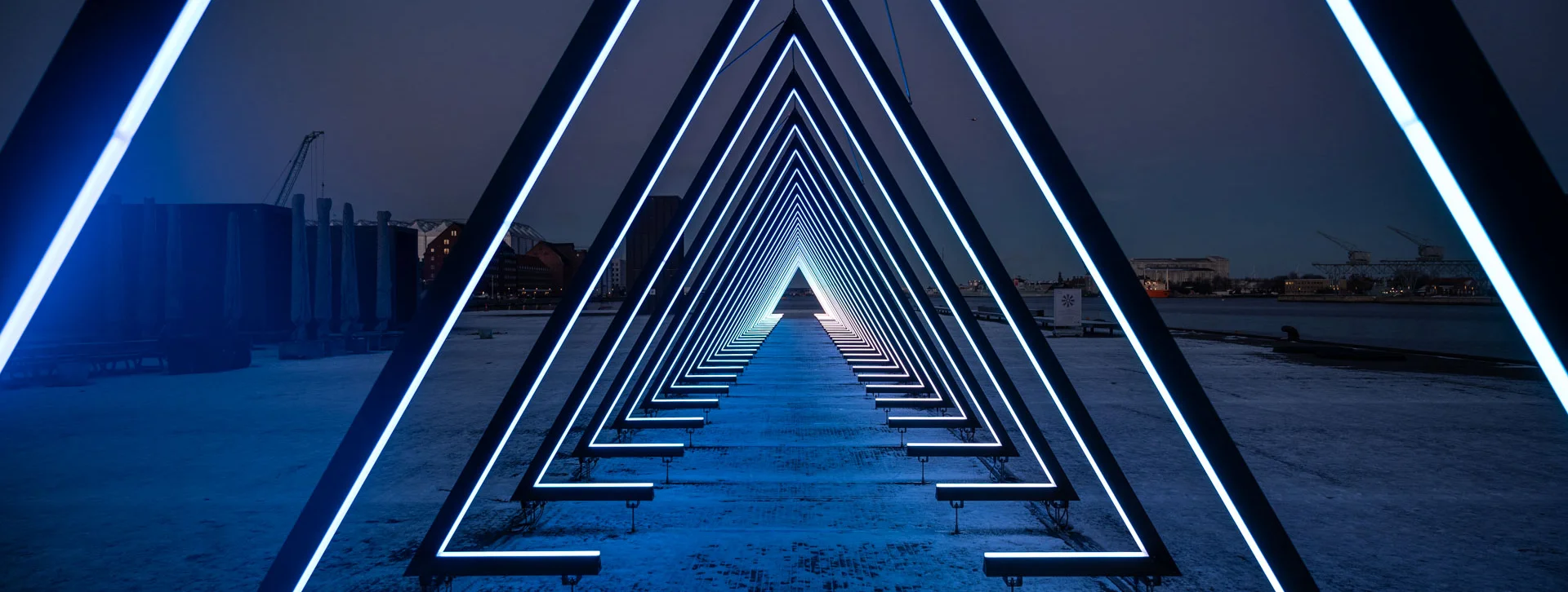 Illuminated triangular arches forming a tunnel over a snowy path at night.