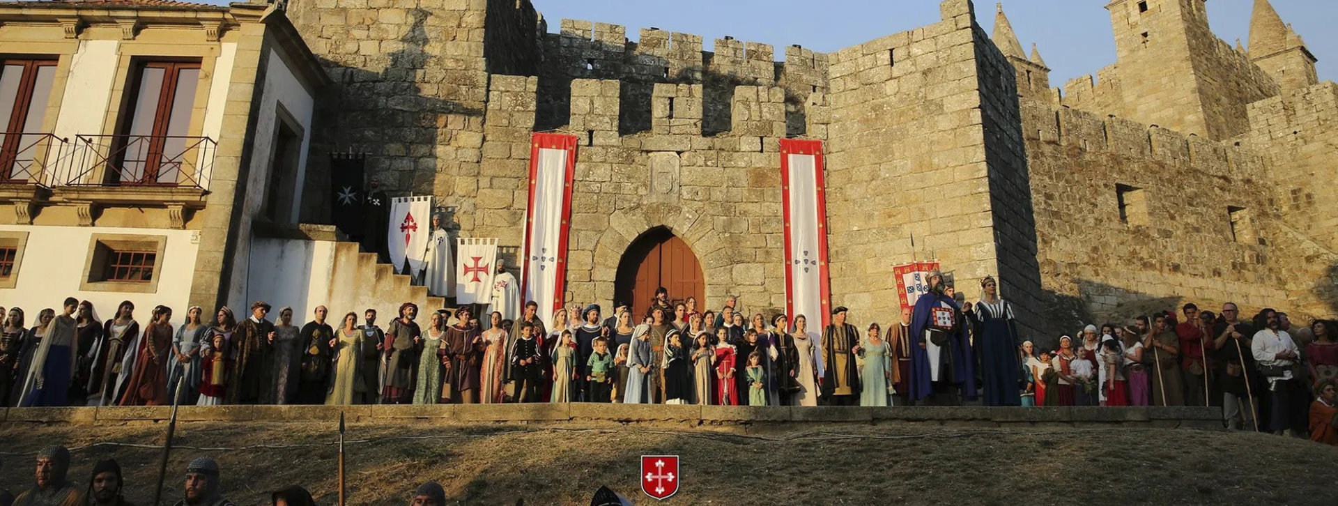 People in medieval costumes gathered outside a stone castle during a festival.