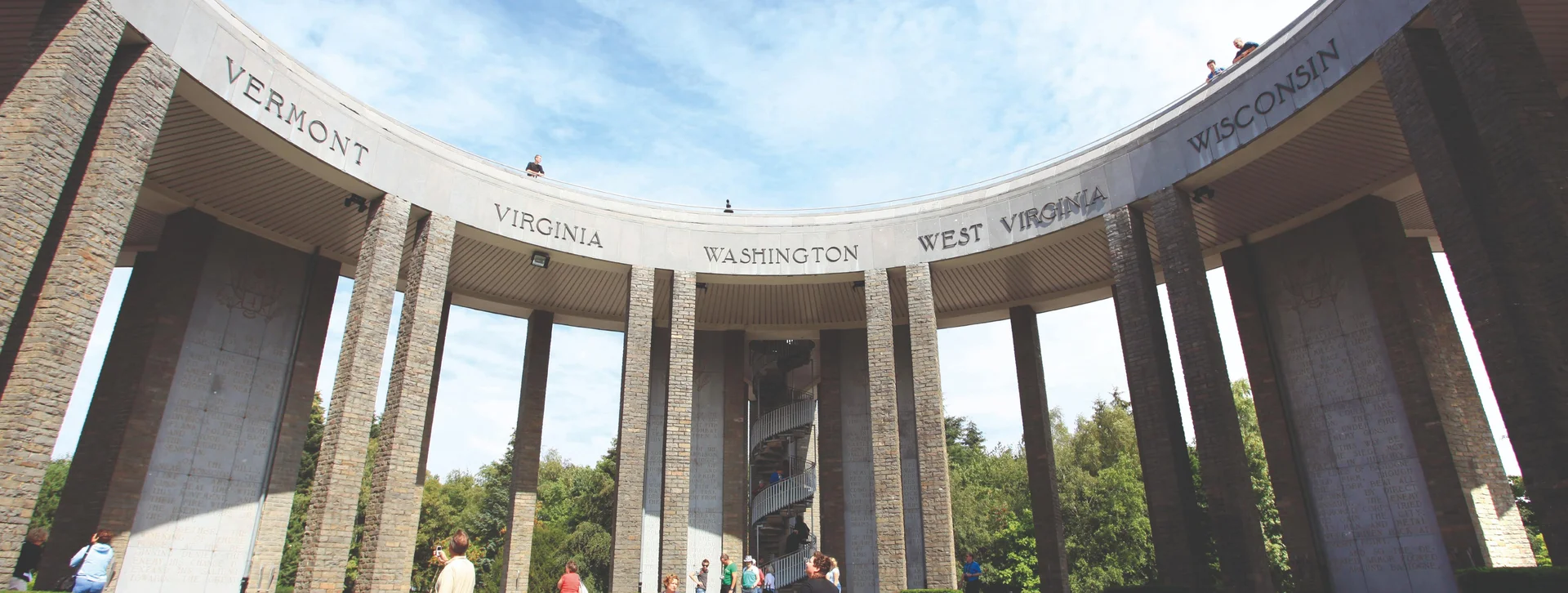 People standing inside a circular stone monument with tall columns under a blue sky.