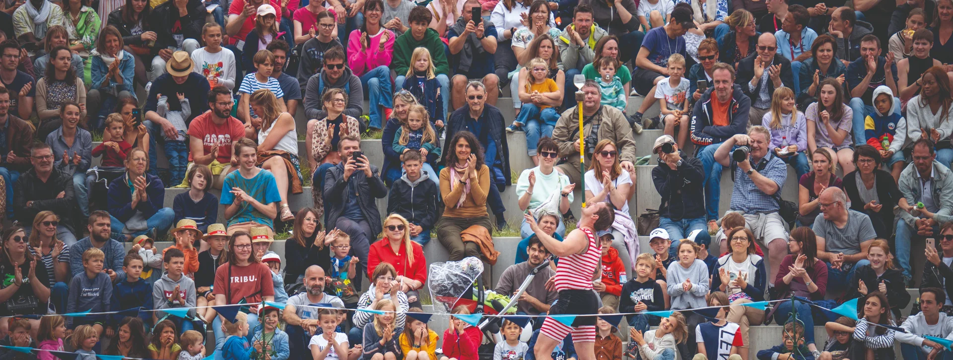 Performer juggling on stage before a large, diverse outdoor audience.