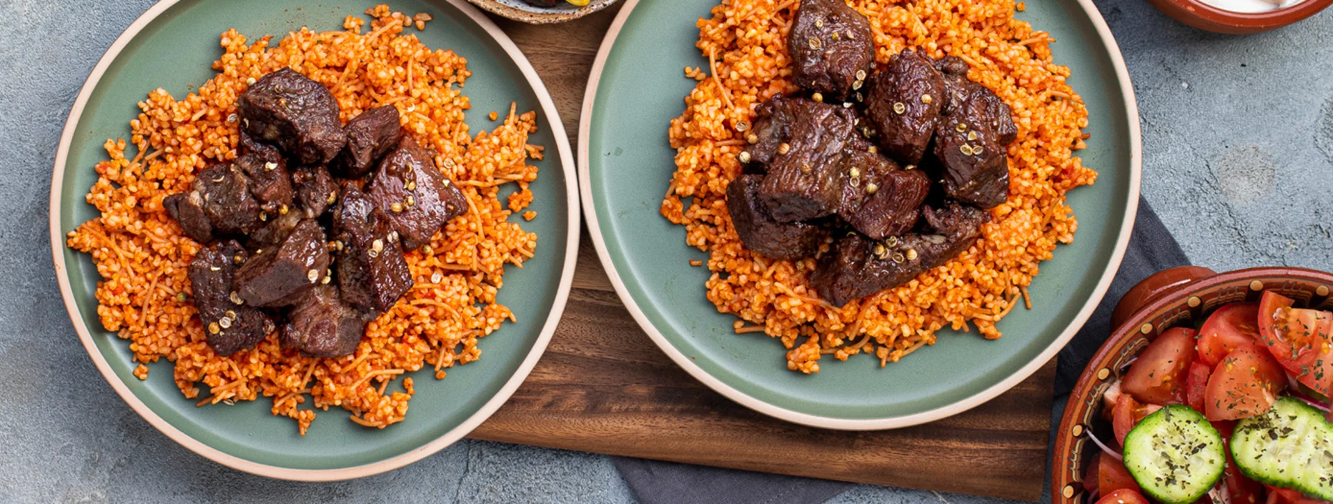 Two plates of orange rice topped with chunks of meat, with a salad on the side.