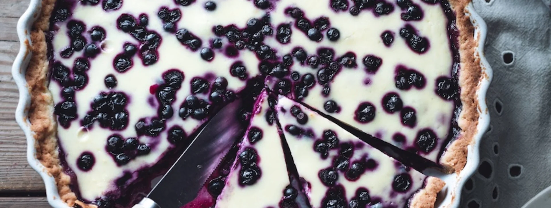 Blueberry tart with a slice cut out, served on a rustic wooden table.