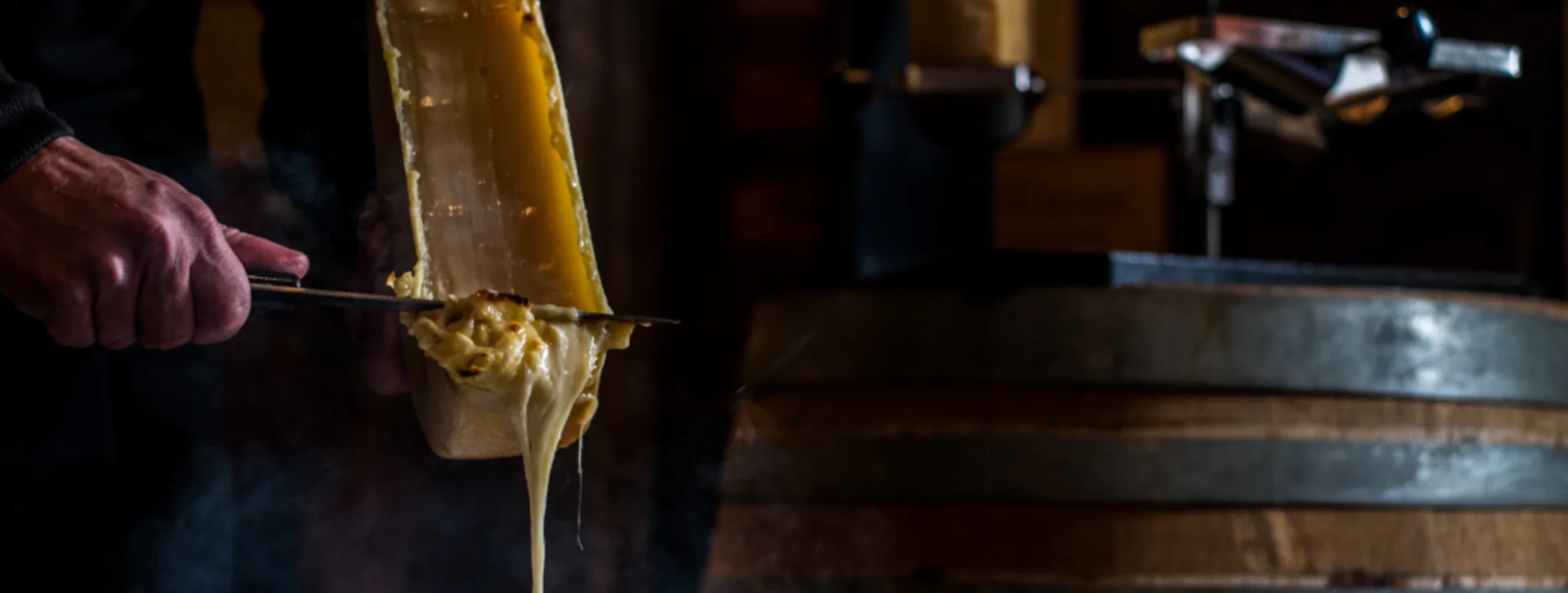 Melted raclette cheese scraped onto a plate of potatoes, with a rustic wooden barrel in background.