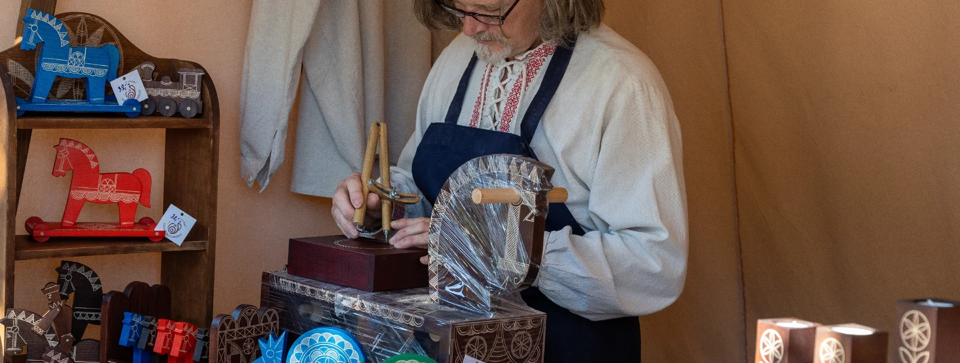 Woman working on wooden crafts at a market stall with colorful carved horses.
