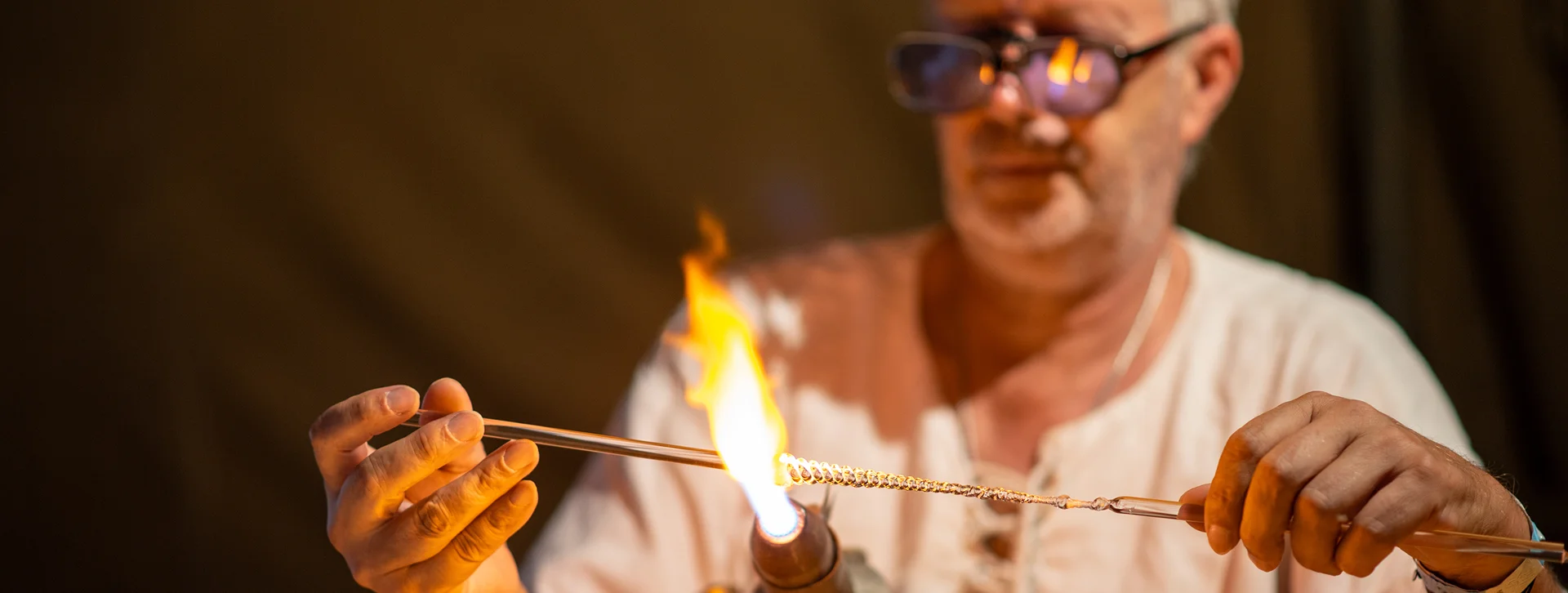 Man wearing glasses shaping glass with a torch flame.