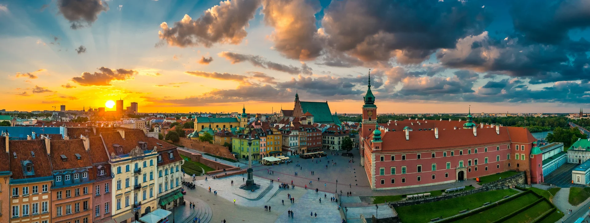 Colorful city square with historic buildings at sunset, sun rays shining through clouds.