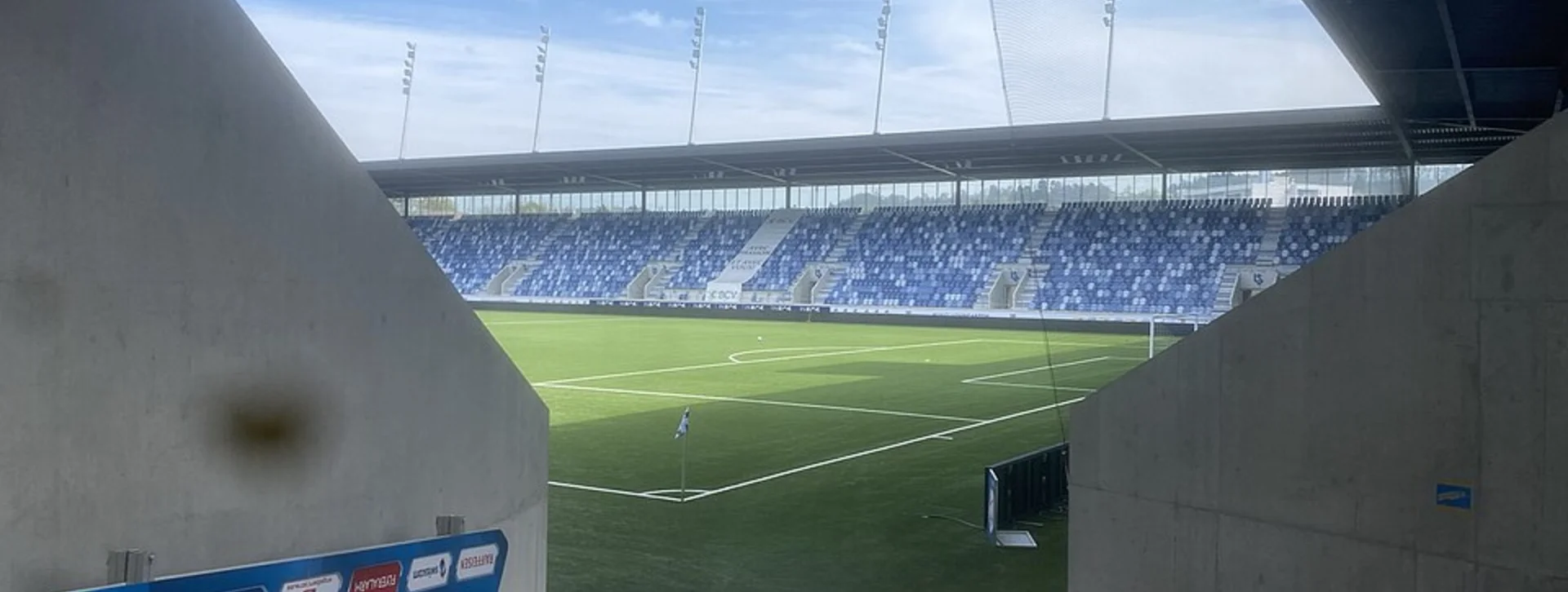 Entrance tunnel view of an empty soccer stadium with green field and blue seats.