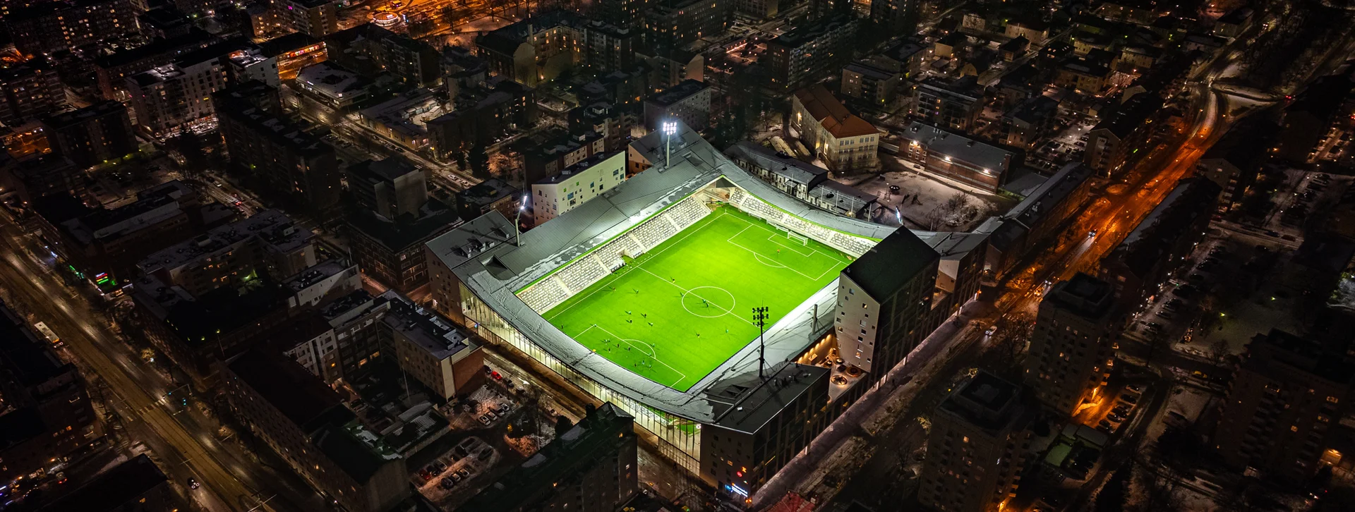 Brightly lit football stadium surrounded by city buildings at night.