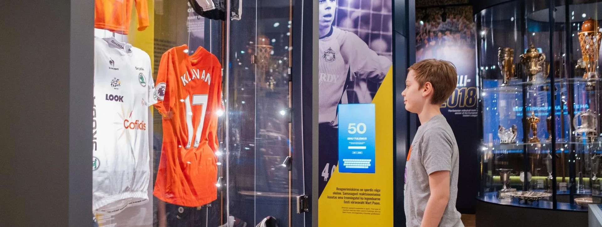 Young boy looking at sports jerseys and trophies in a museum display.