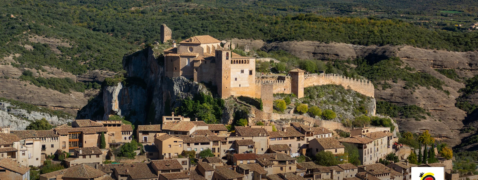 Medieval castle on a hilltop surrounded by old village houses and green forested hills.