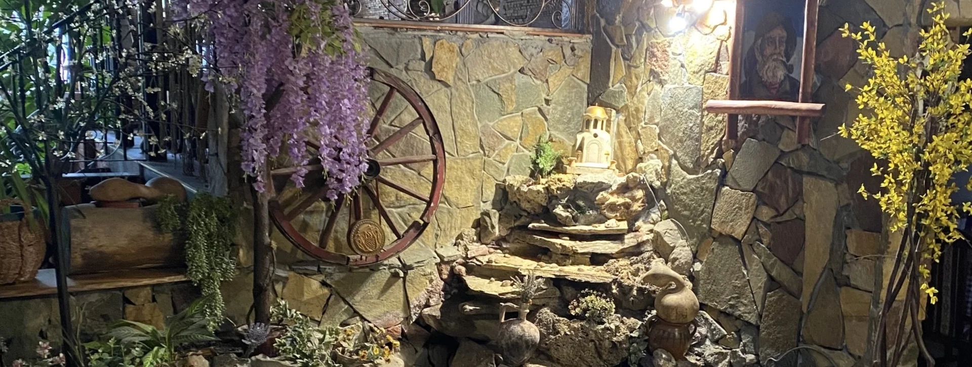 Small indoor rock fountain surrounded by plants and rustic decor, including a wagon wheel.
