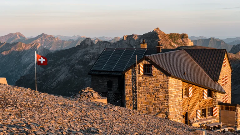A house surrounded by mountains and a Swiss flag.