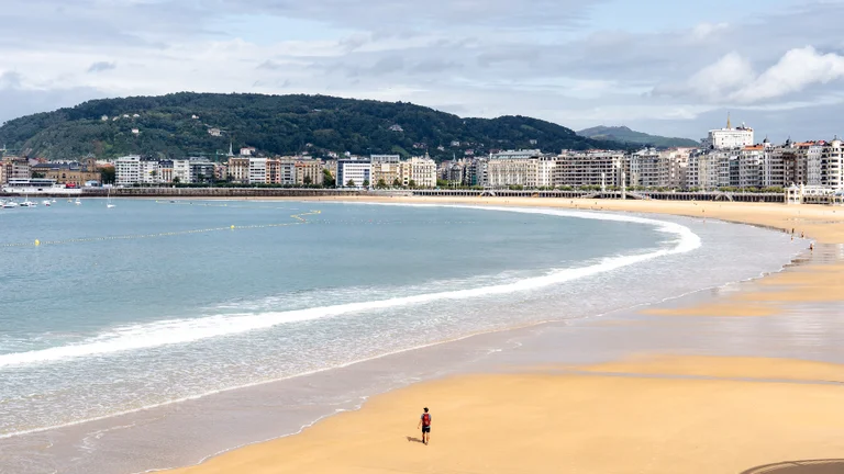 A stunning beach with yellow sand, the blue sea and a mountain with houses around to complement the landscape.