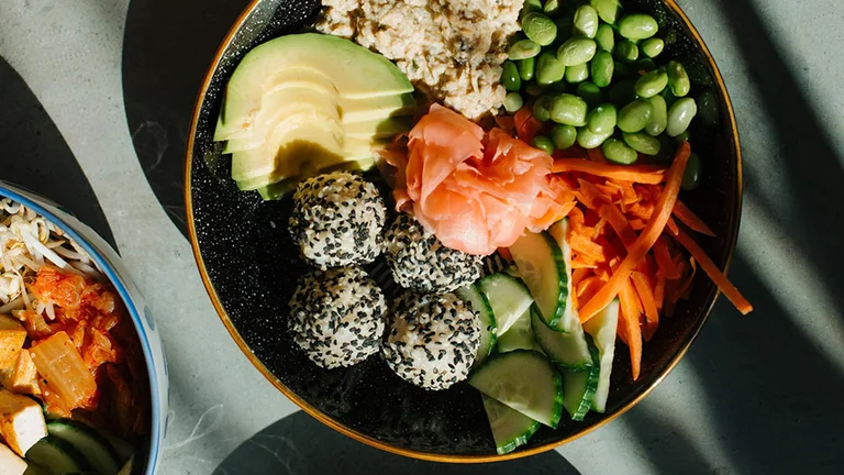 How about a beautifully arranged vegan bowl featuring avocado slices, edamame beans, pickled ginger, shredded carrots, cucumber, and sesame-covered rice balls at Wild Kitchen?