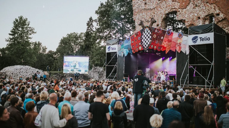 A crowd enjoying a concert at the Viljandi Folk Music Festival, with a stage set against the backdrop of historic stone ruins, decorated with colorful patterns.