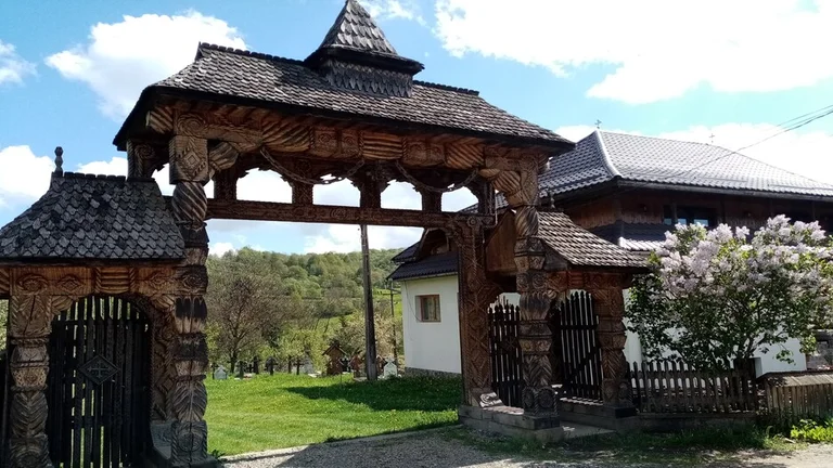 Ornately carved wooden gateway with traditional motifs in a rural setting in Breb village, Romania.